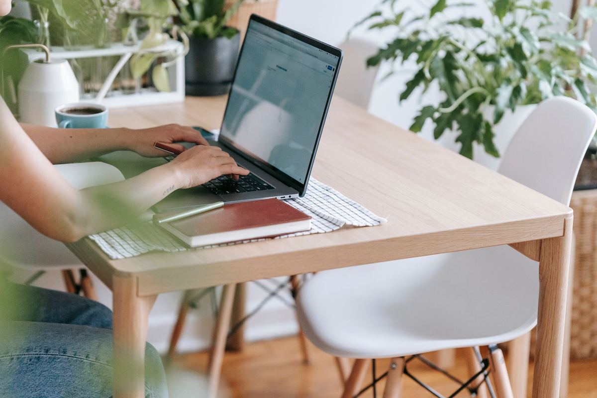 A woman typing on a laptop at a light wooden desk surrounded by houseplants