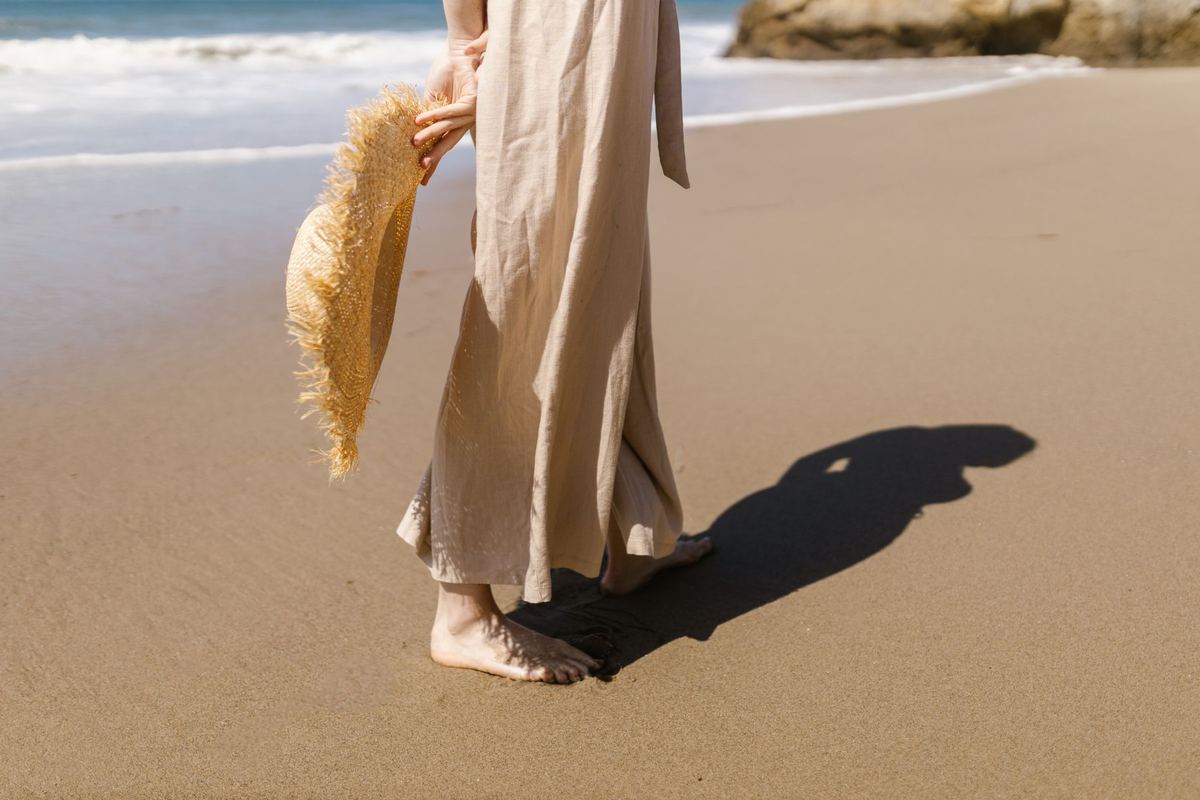 A woman in linen trousers walking barefoot along the shoreline
