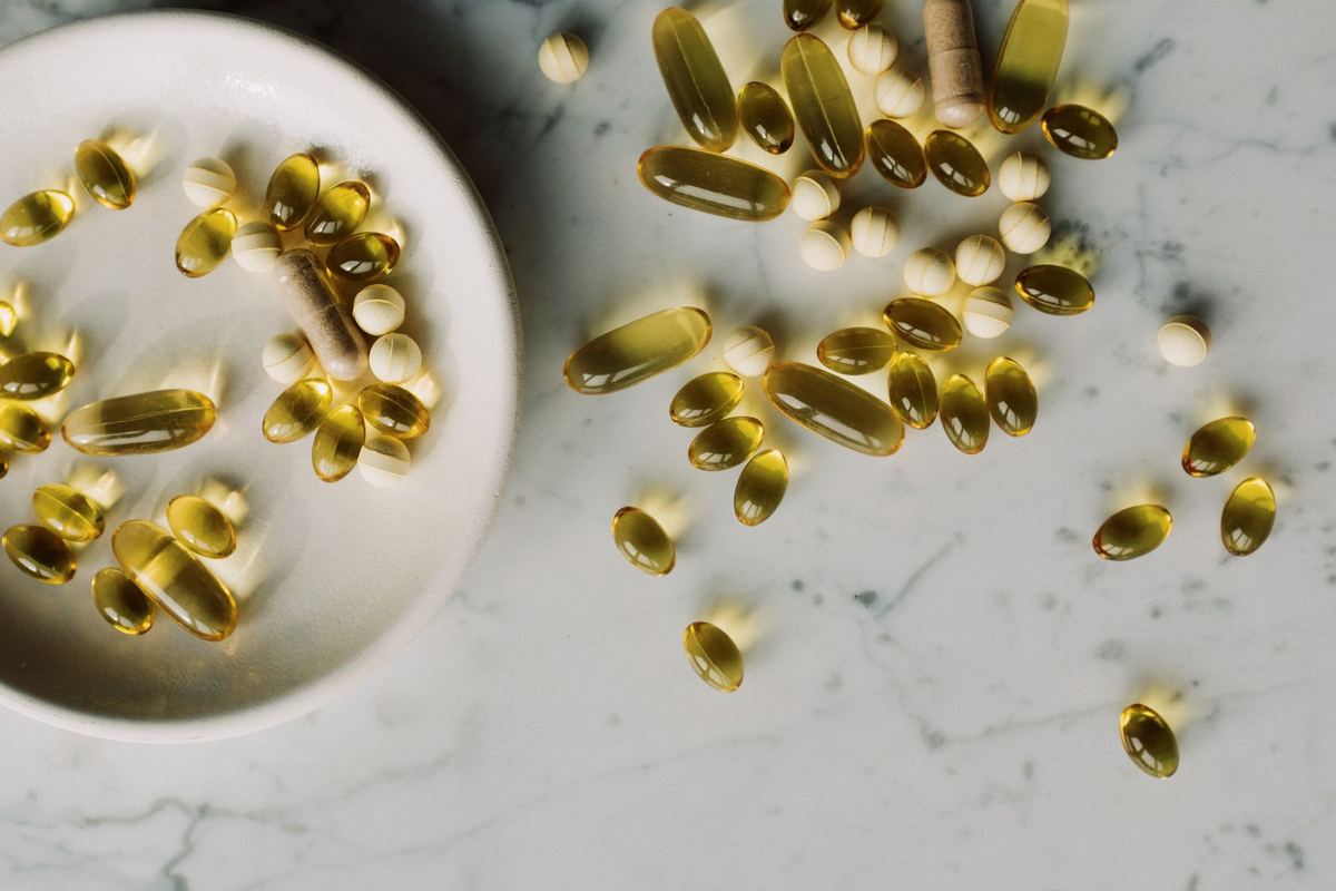 Golden softgel capsules on a white marble surface beside a ceramic dish